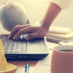 Hands of architect holding coffee cup and working on laptop