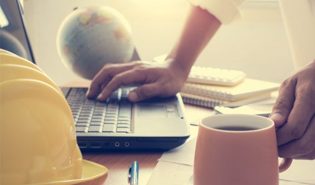 Hands of architect holding coffee cup and working on laptop